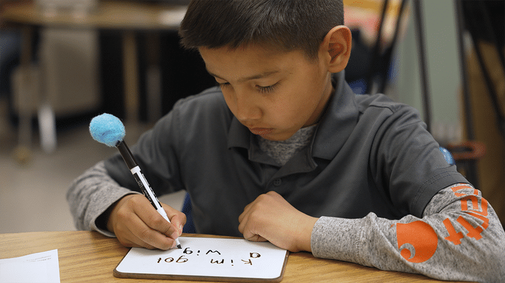 A student writes out words with short vowels on a wipe board