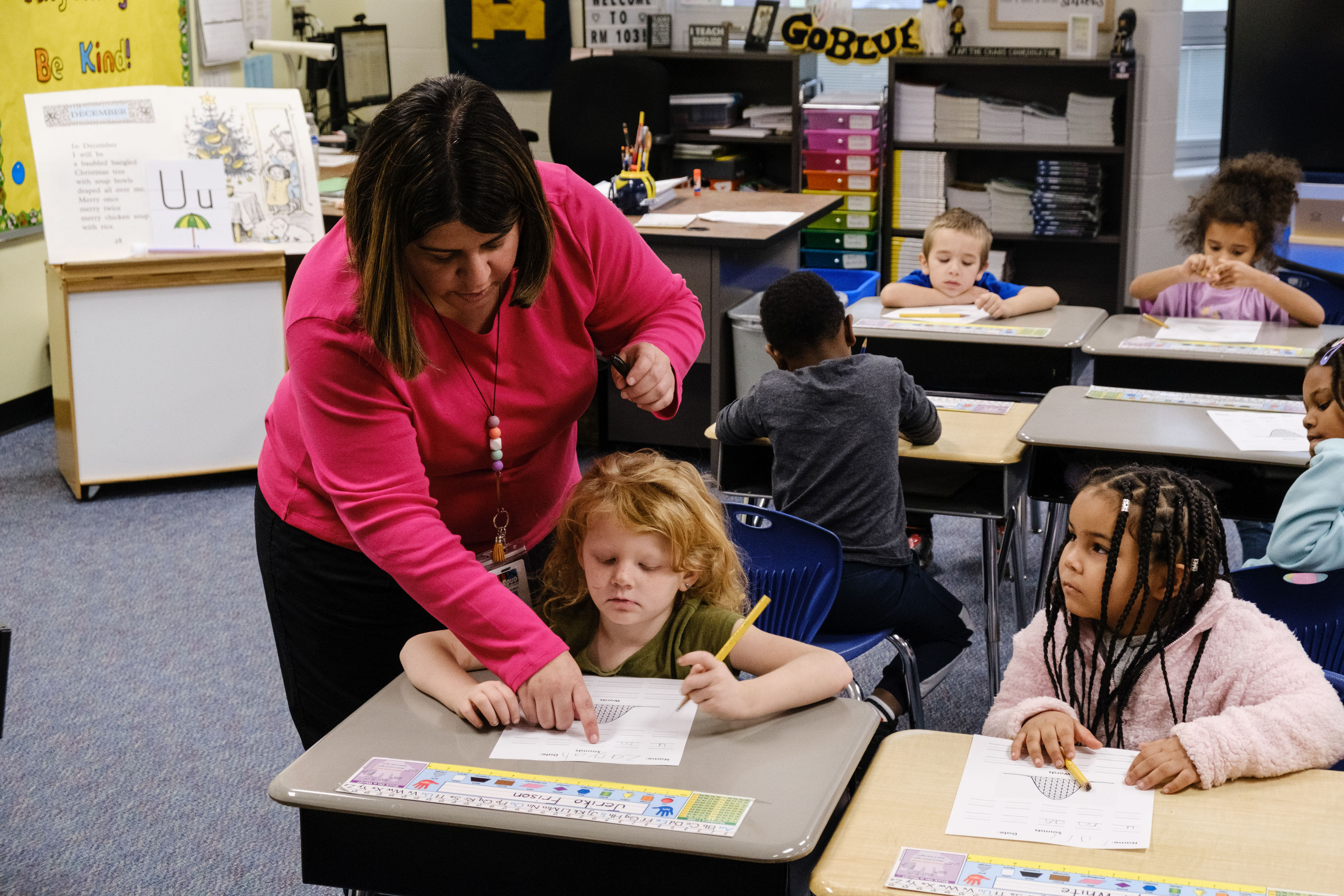 Teacher supports student at desk during whole group phonics instruction