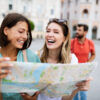 Holidays, travel, friends and tourism concept. Beautiful girls looking into tourist map in the city