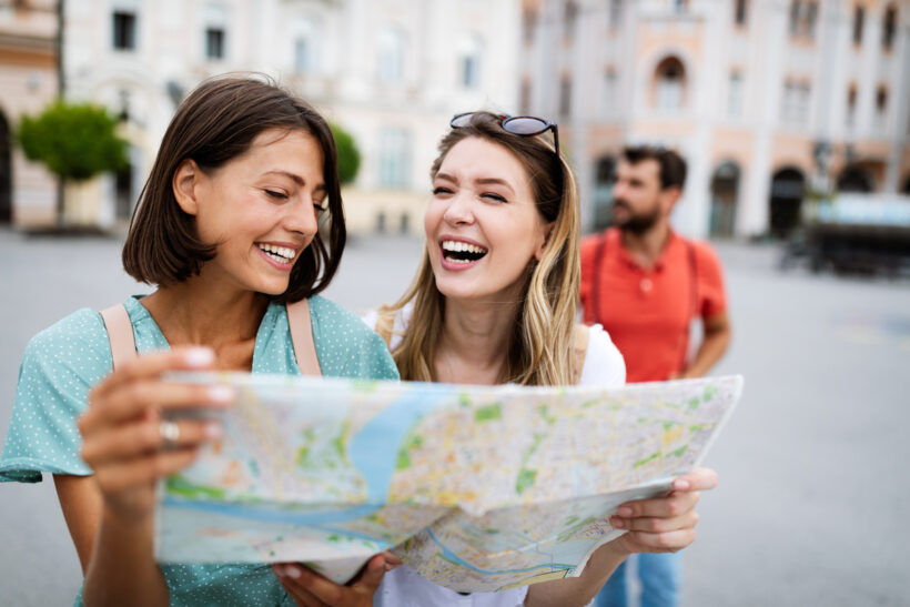 Holidays, travel, friends and tourism concept. Beautiful girls looking into tourist map in the city