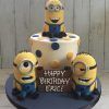 Three minions on and around a cake with polka dots