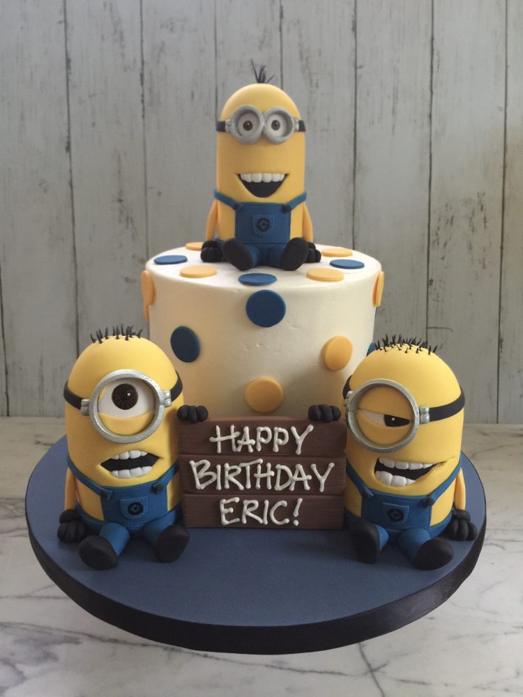 Three minions on and around a cake with polka dots