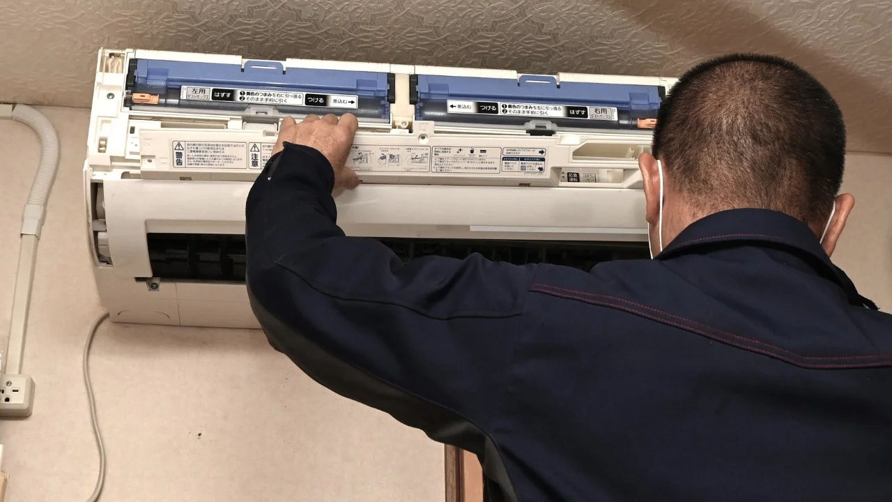 Technician repairing an air conditioner unit in New Delhi workshop.