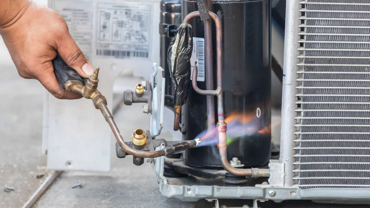 Technician repairing an air conditioner unit outdoors, wearing a facemask and using a manifold gauge.