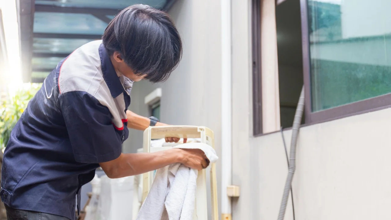Technician repairing an air conditioner unit in New Delhi workshop.
