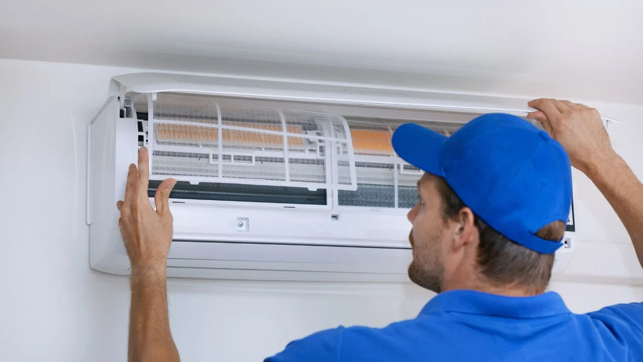 A technician skillfully repairing an outdoor air conditioning unit mounted on a building wall.