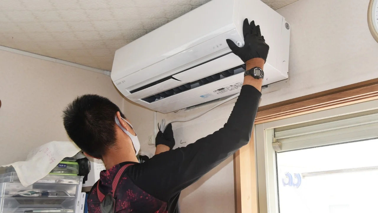 Technician repairing an air conditioner unit outdoors, wearing a facemask and using a manifold gauge.