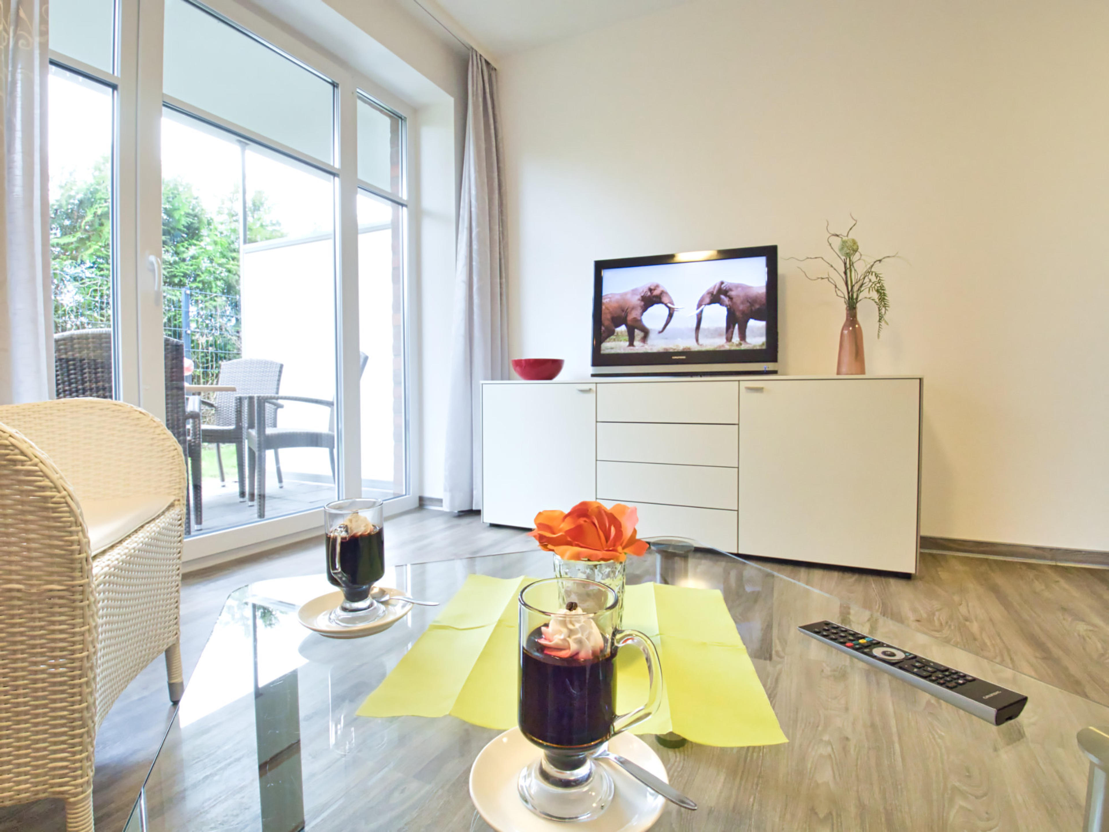 Wohnzimmer mit Glastisch,  Korbsessel, Sideboard und Flatscreen TV, Terrassentür
