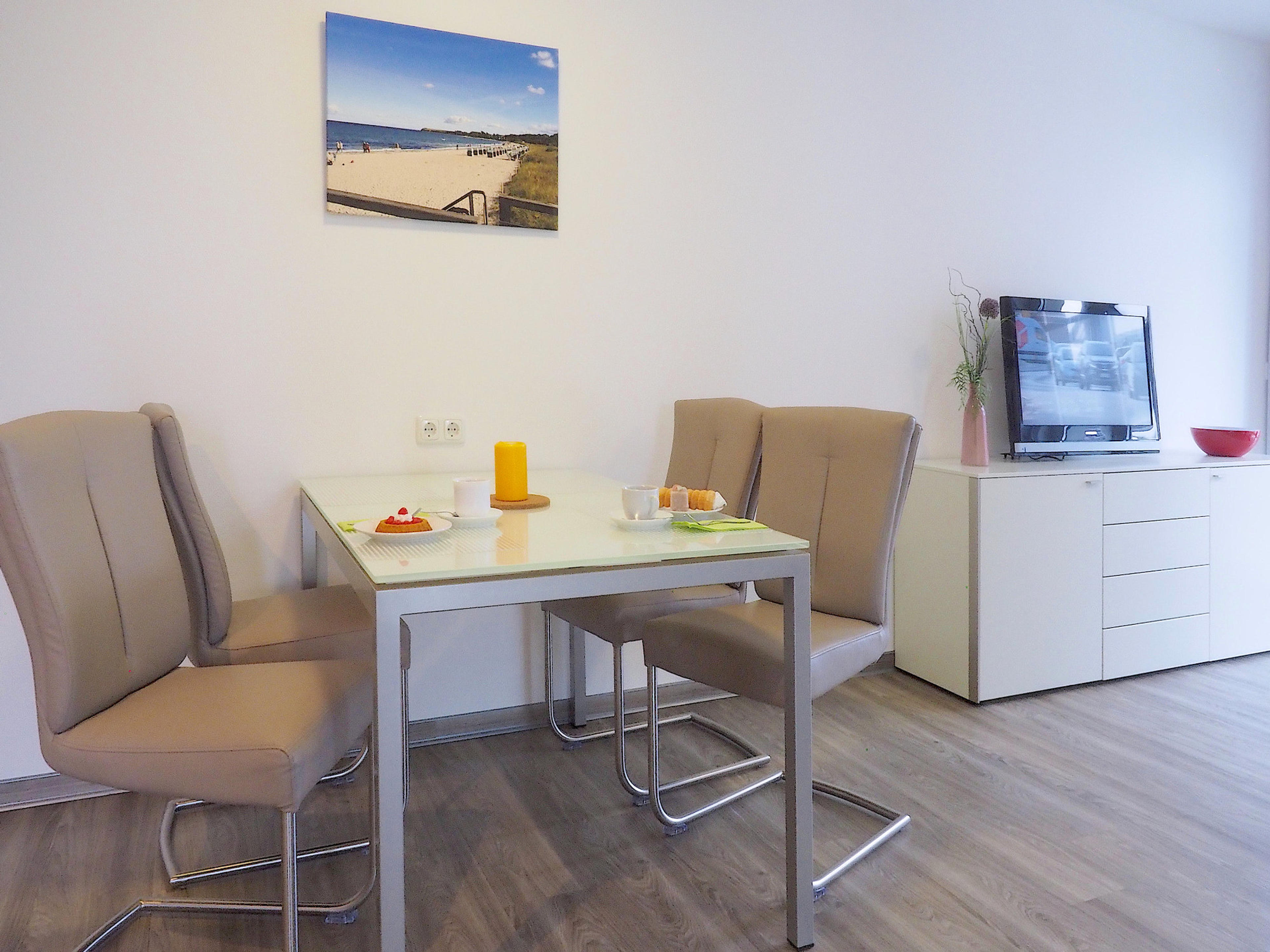 Esstisch mit 4 Stühlen, rechts davon Sideboard mit Flatscreen TV 
