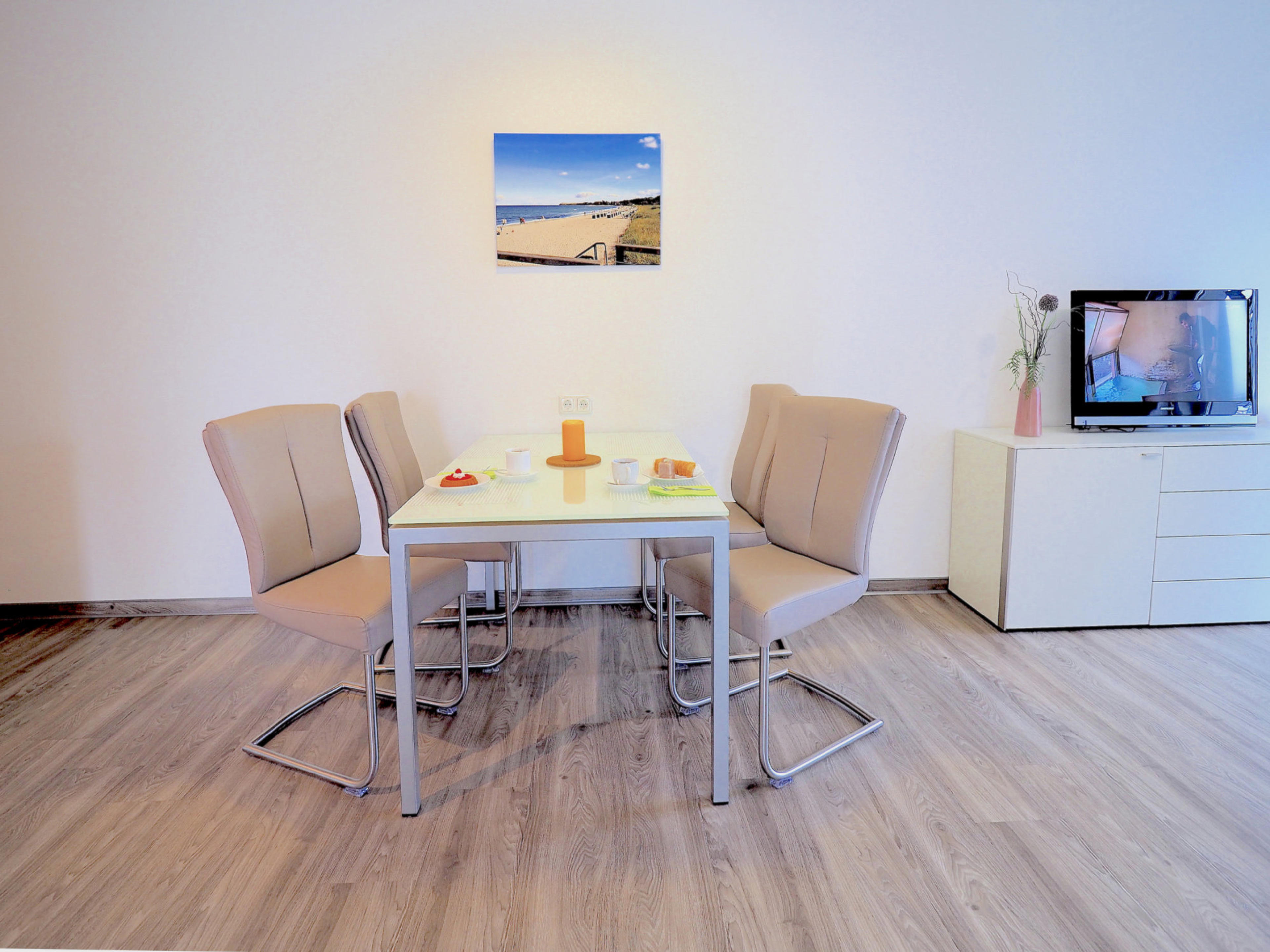 Esstisch mit 4 Stühlen, rechts davon Sideboard mit Flatscreen TV 
