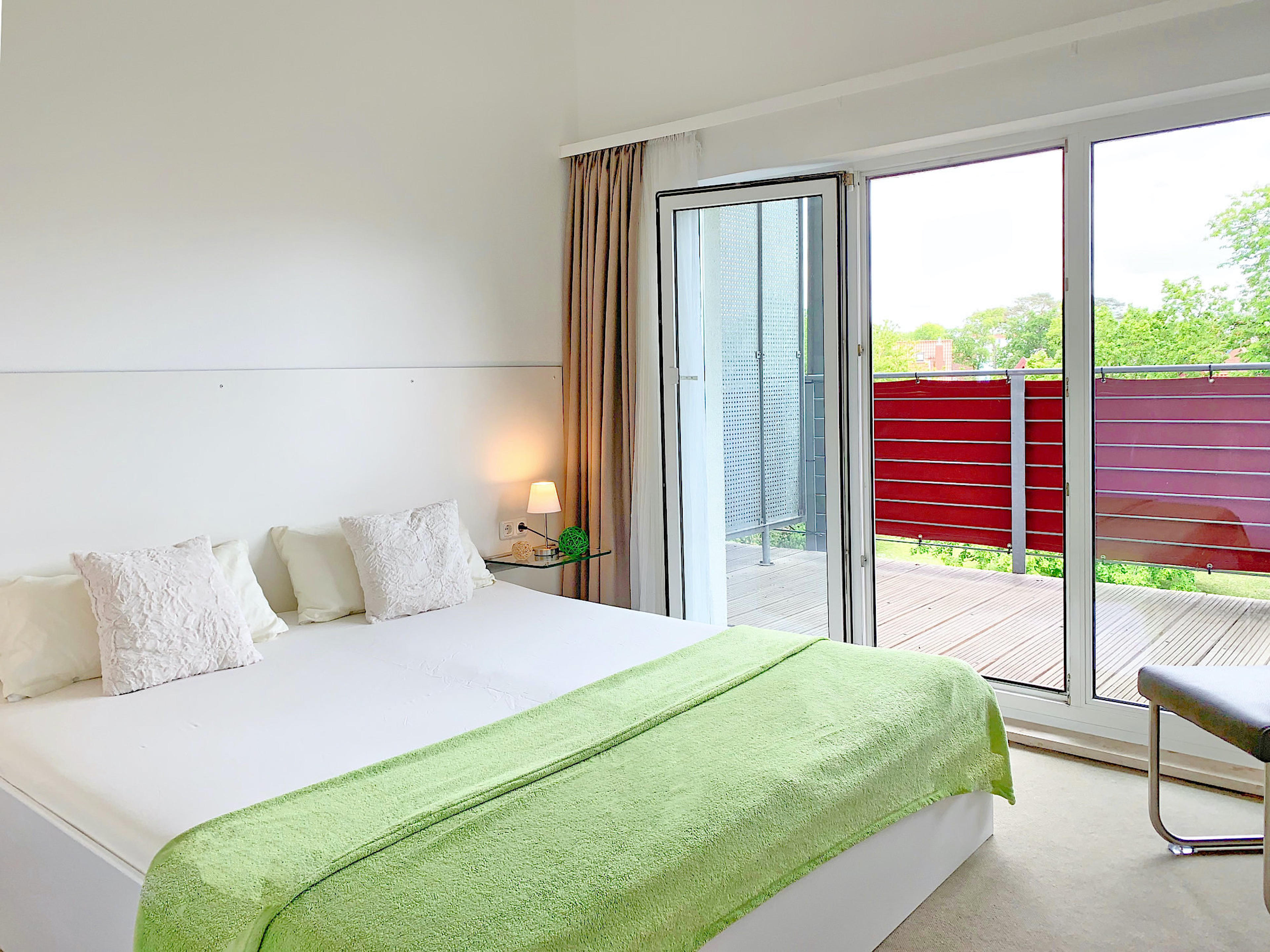 Schlafzimmer mit Doppelbett, rechts davon bodentiefe Fenster und Zugang zum Balkon
