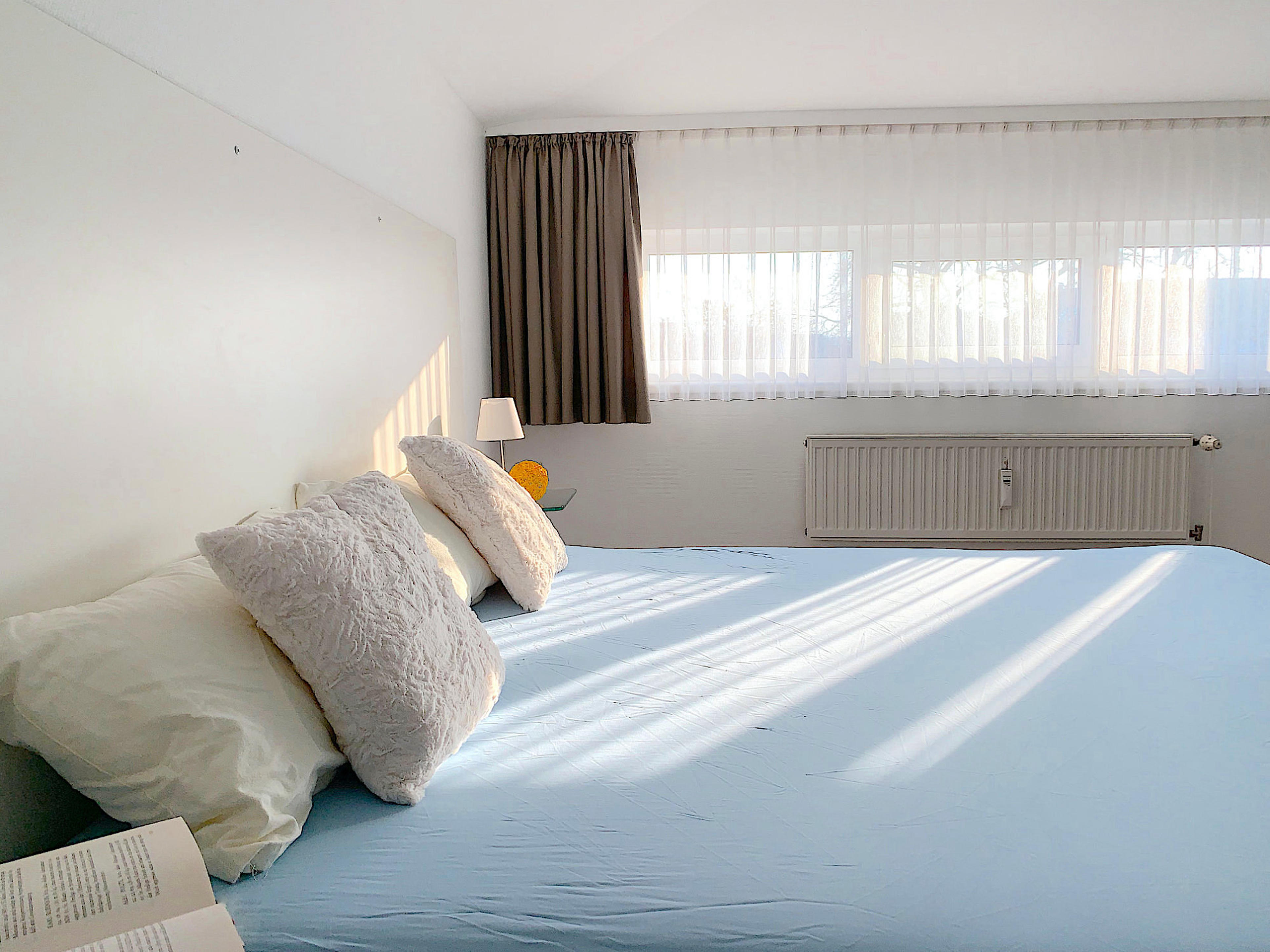 Schlafzimmer mit Doppelbett, rechts davon ein großes Fenster
