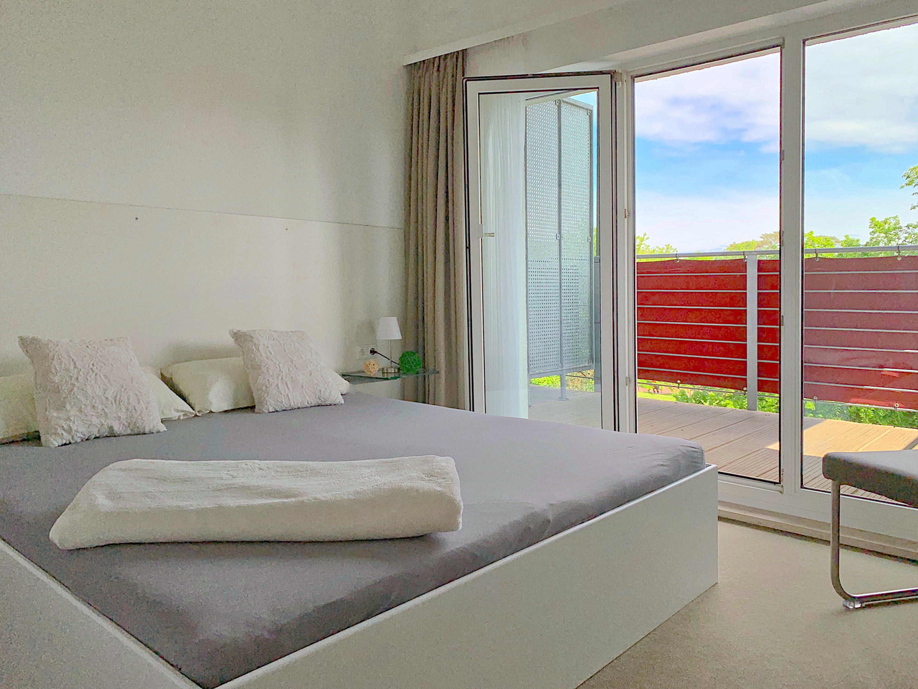 Schlafzimmer mit Doppelbett, dahinter bodentiefe Fenster mit Balkon