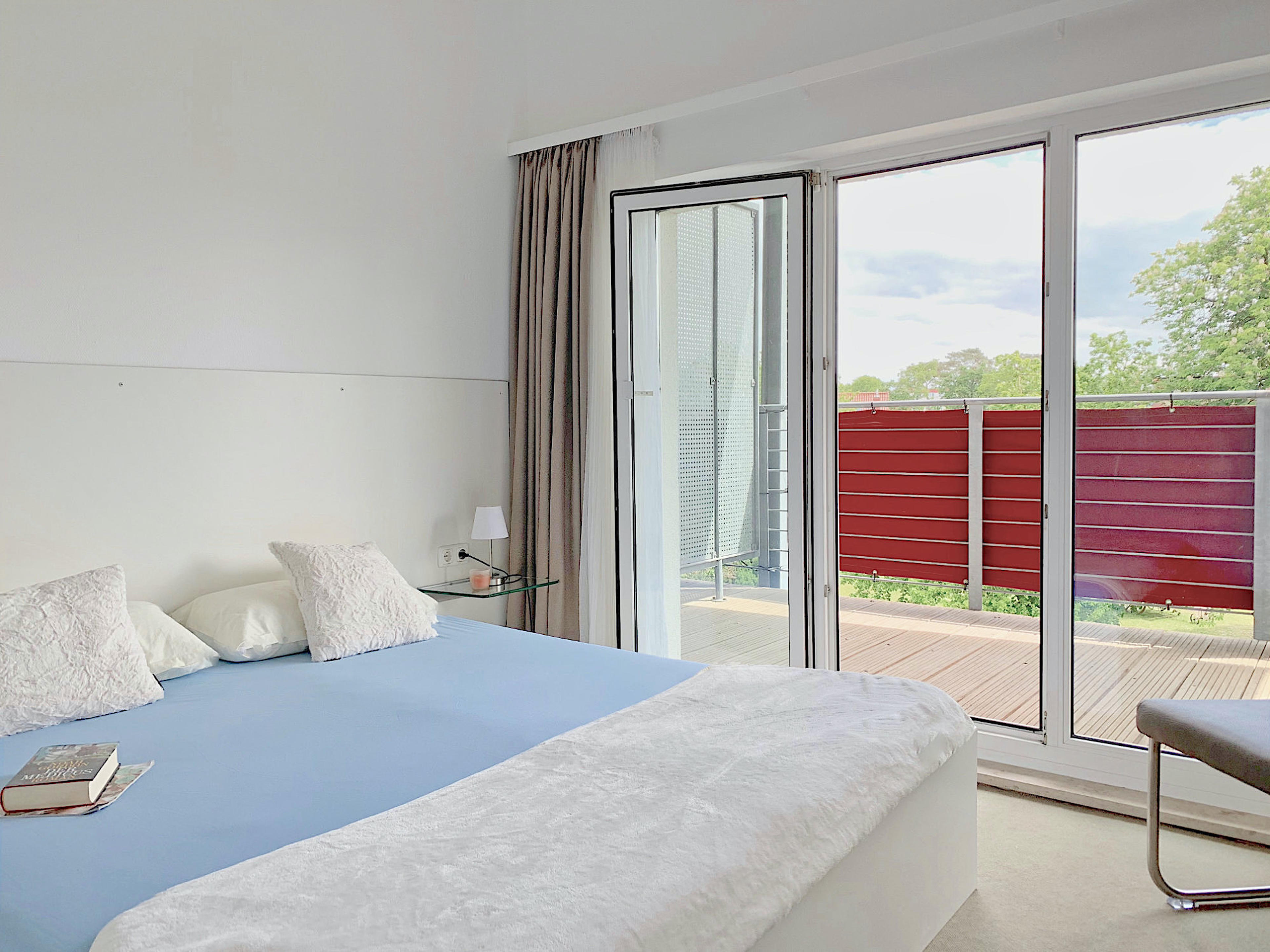 Schlafzimmer mit Doppelbett, rechts davon bodentiefe Fenster und Zugang zum Balkon
