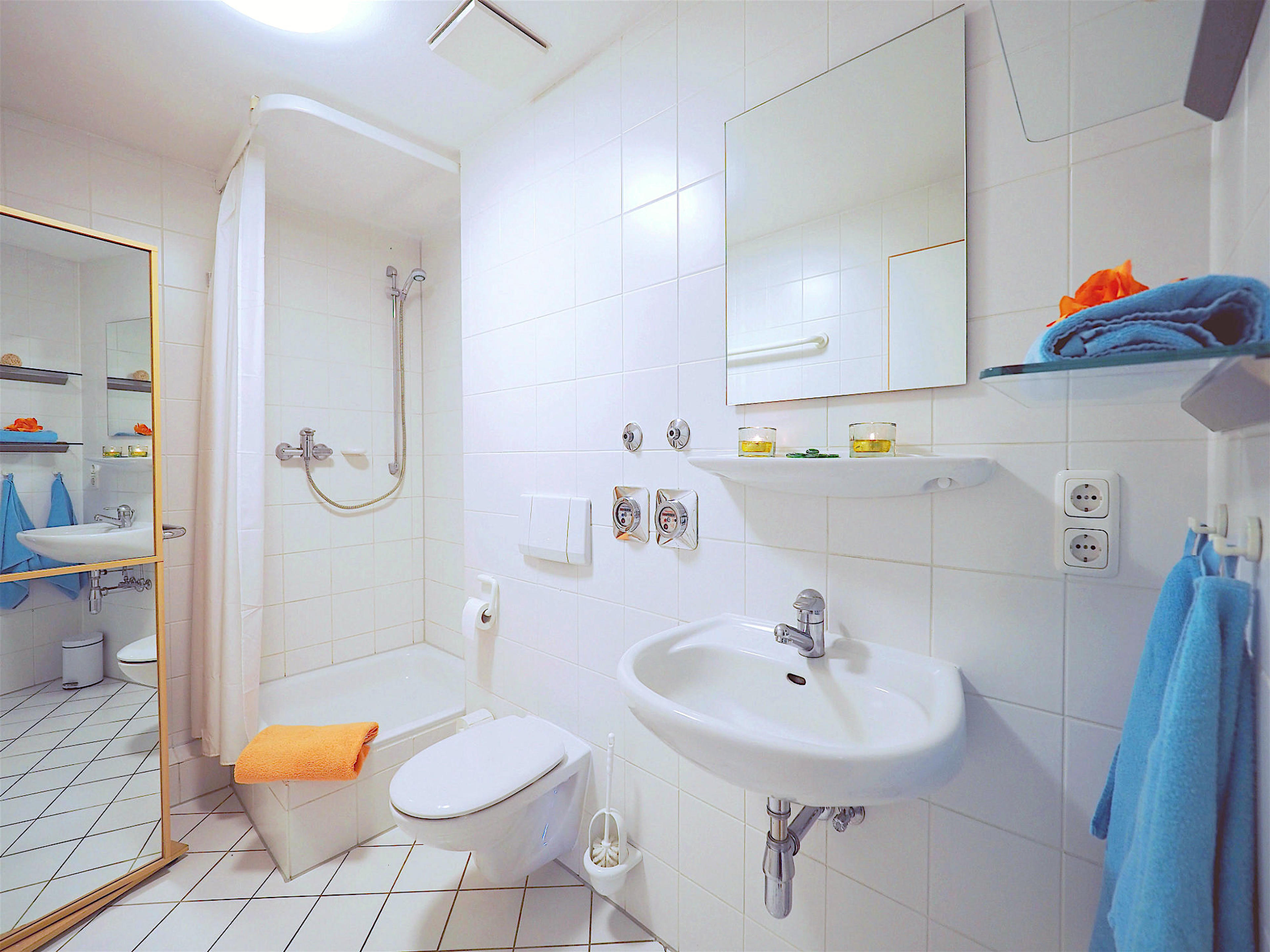 Duschbad mit mit Dusche, links davon ein Waschbecken mit Spiegel, auf der rechten Seite ein Hochschrank mit Spiegelfront 

