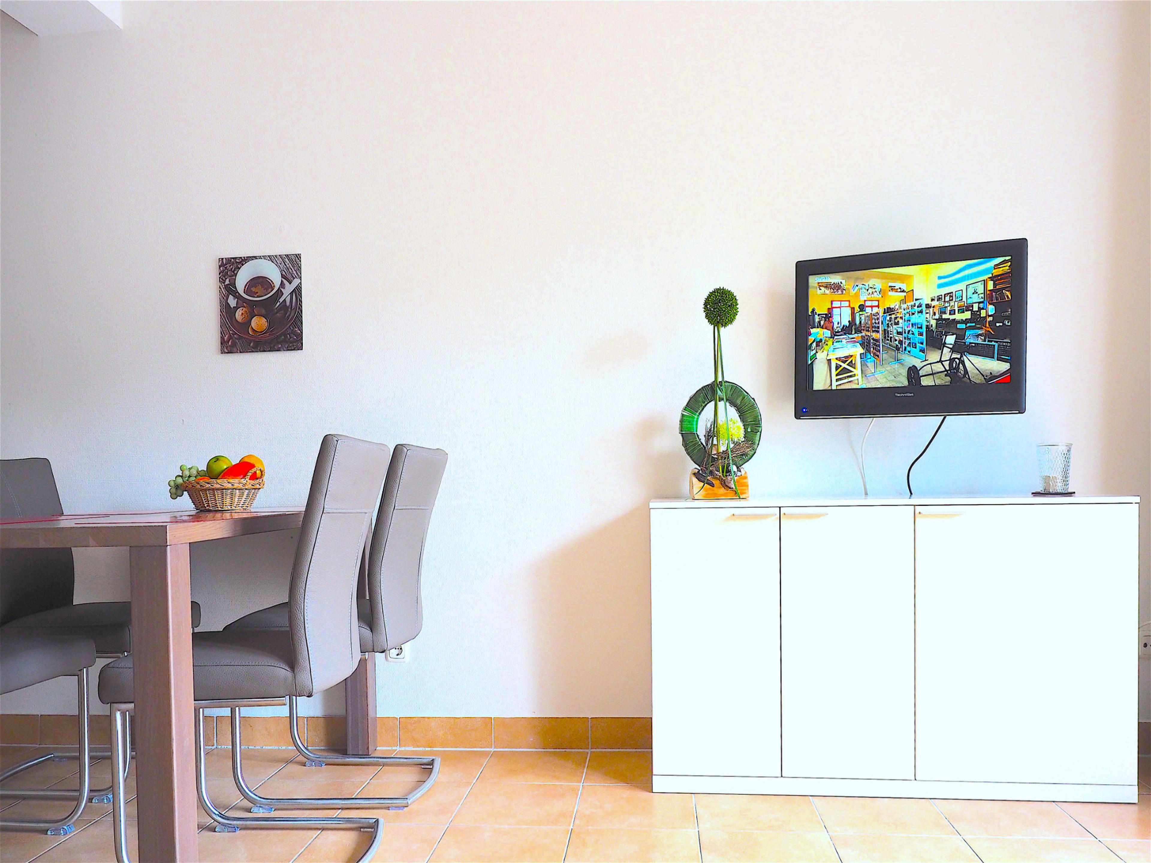 Wohnzimmer, links der Esstisch mit Stühlen, rechts ein Sideboard mit Flatscreen TV und Deko