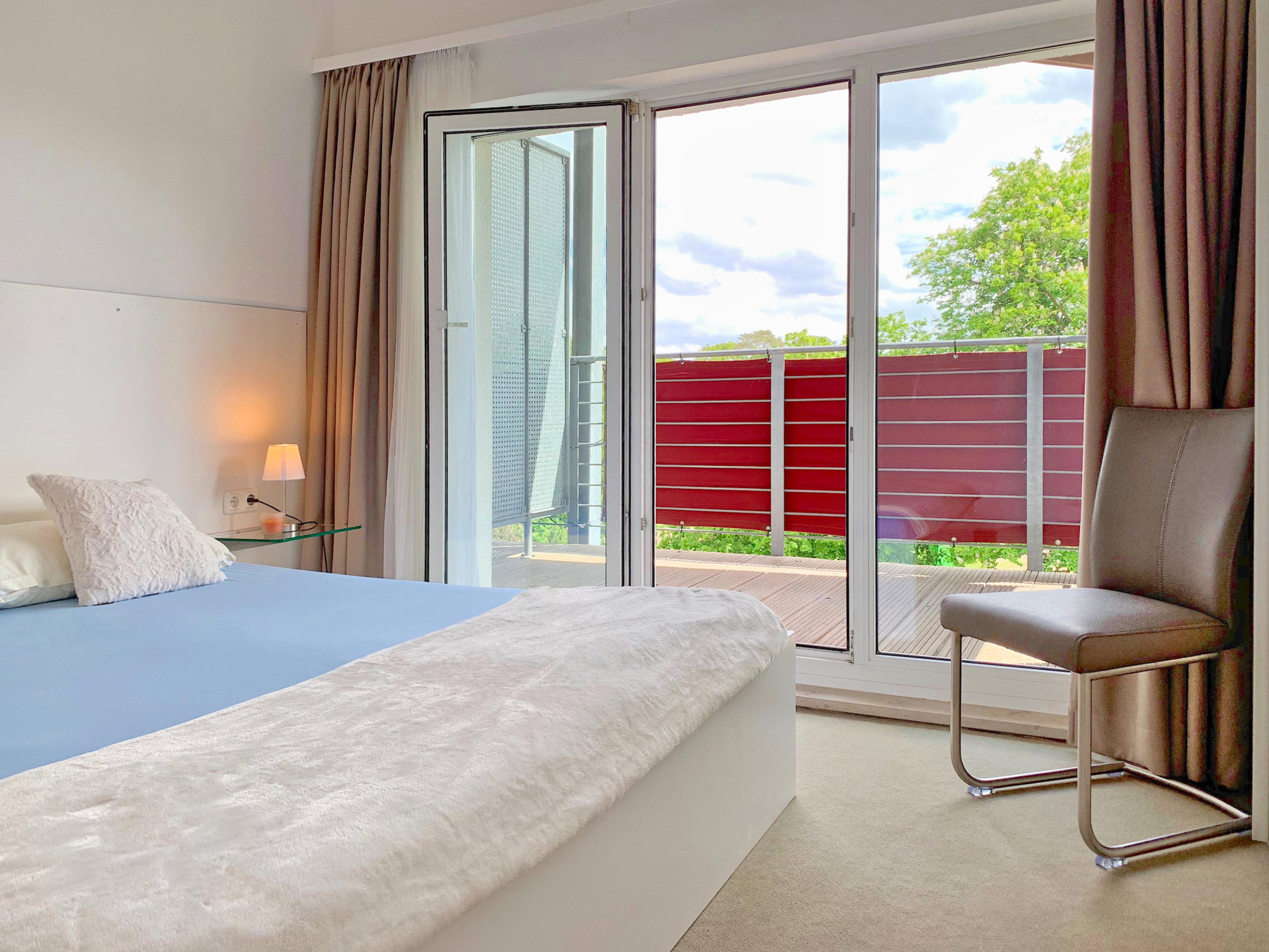 Schlafzimmer mit Doppelbett, rechts davon bodentiefe Fenster und Zugang zum Balkon
