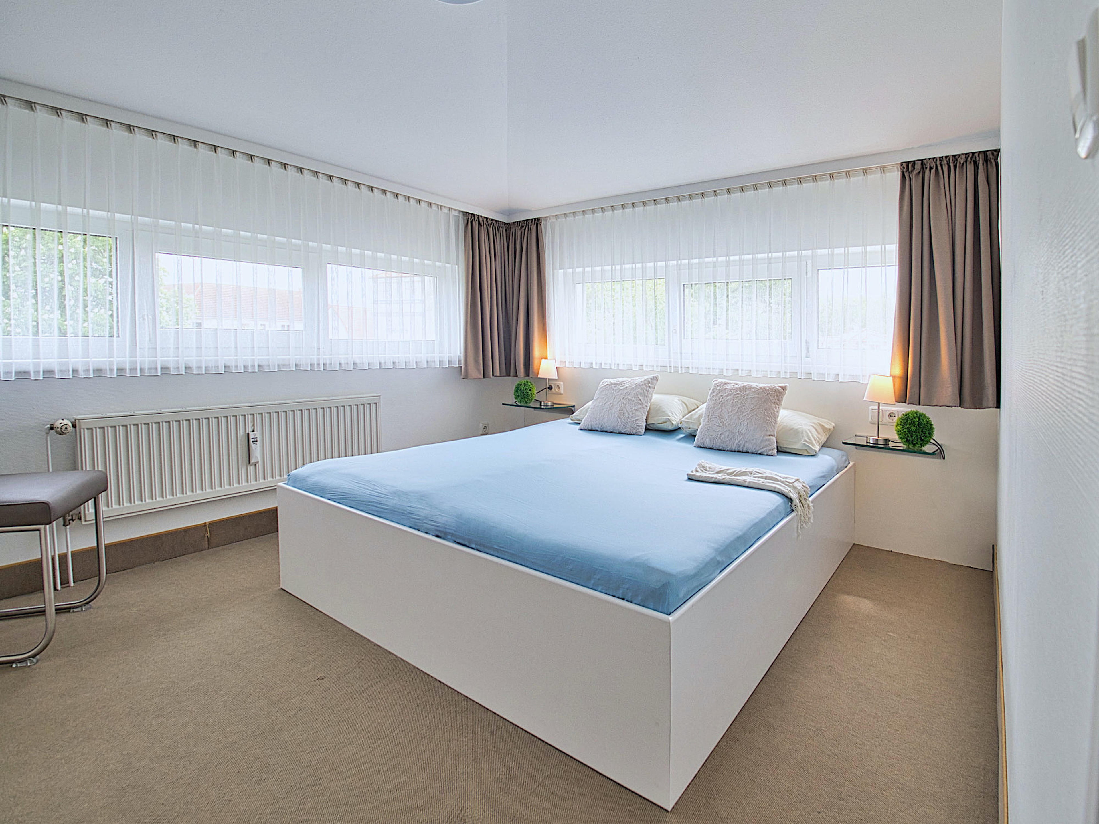 Schlafzimmer mit Doppelbett, an zwei Wänden jeweils 2 Fenster
