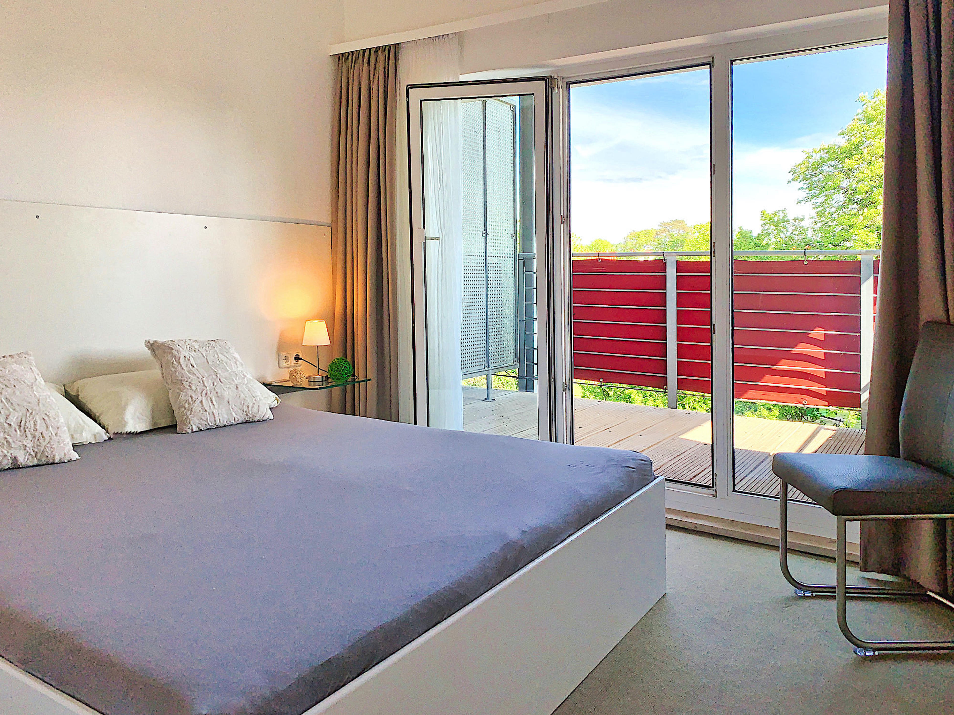 Zweites Schlafzimmer mit Doppelbett, rechts davon bodentiefe Fenster und Zugang zum Balkon
