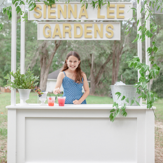 White lemonade stand with smilax and little girl server at Sienna Lee Gardens.