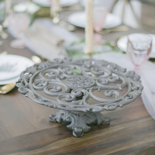 Ornate metal wrought cake stand on wood table with candles and pink glasses.