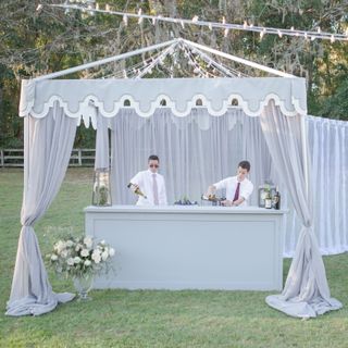 Bartenders with grey wedding bar under grey tent for outdoor reception.