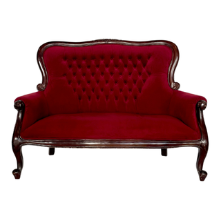 Vintage velvet tufted red loveseat with dark brown wood accents outdoors with a couple sitting on it embraxing. 