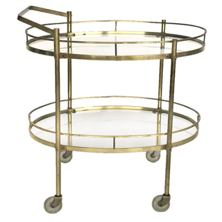 Vintage gold metal oval tea cart with a pink drape and desserts with floral arrangements surrounding it. Several side tables surround it with sweets and desserts on it. A gold arch with a pink purple drape on one side and a floral arrangement on the other