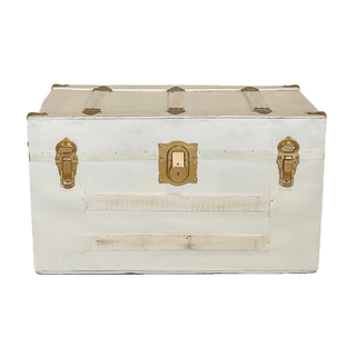 Vintage whitewashed rectangular trunk coffee table with gold accents with ab briefcase and decor on top of it in the corner of a large blue linen table filled with desserts, favors and a tiered cake. Aside the large table are two tufted armchairs, one pin