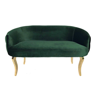 Modern mid-century velvet hunter emerald green loveseat with gold legs in a lounge set with red tufted vintage chairs, gold and round coffee table over a red patterned rug. 