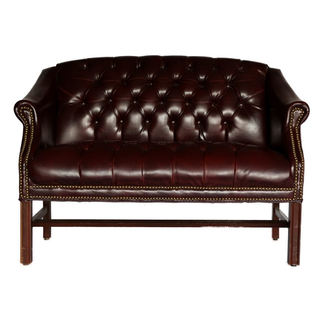 Mid-century vintage leather tufted dark brown loveseat with wood legs in a lounge with tufted ivory and wood chairs, a wood round table, and a beige rug. 