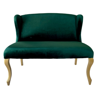 Mid-century velvet emerald green loveseat with gold legs tucked into a wood farm table with a garland and candle decor. 