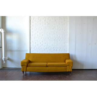 Mid-century yellow sofa with wooden legs and brass accents.