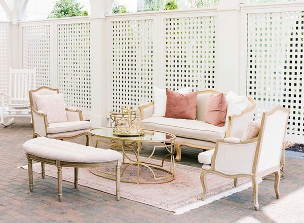 Linen loveseat, two linen chairs, linen bench, gold coffee and side tables with pink pillows and rug 
