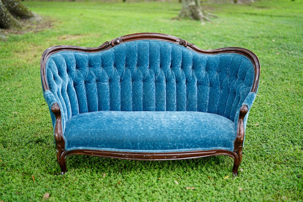 Blue tuffed velvet love seat with brown wood trim and legs