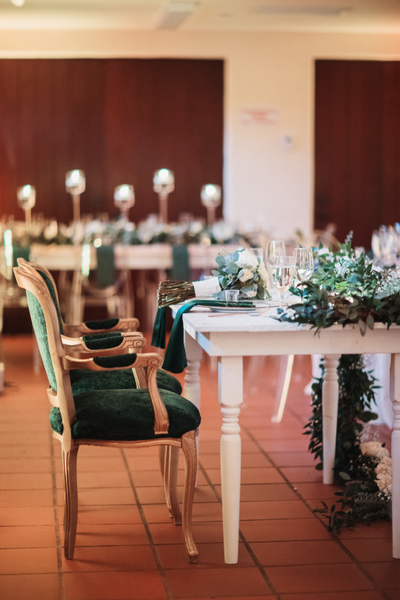 Vintage velvet emerald green arm chair with gold accents tucked into a white wood farm table with garland decor. 