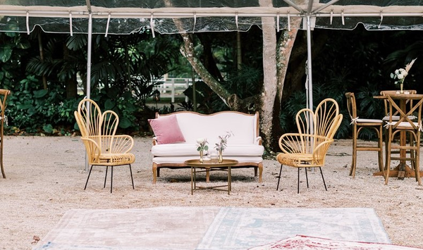 ivory beige loveseat with a bronze round coffee table with boho rattan chairs on either side of the coffee table on a pink  pattern rug. 