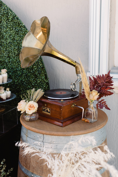 Gold and dark wood vintage gramaphone on a vin barrel with metal accents and floral decor surrounding it. 