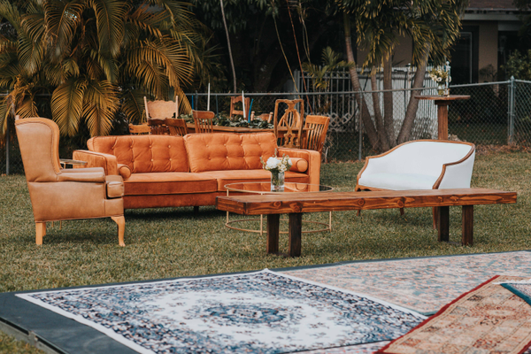 Vintage velvet tufted burnt orange terracota arm chair with wood accents in a lounge set with a white and wood loveseat, large wood bench, and leather tan arm chair. 