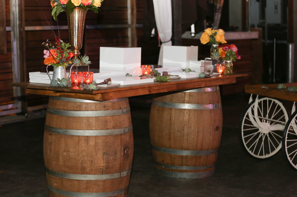 Midwest rustic wood rectangular barrel bar with floral arrangements on top and flickering lights. there are several flickering candles and boxes and trays. 