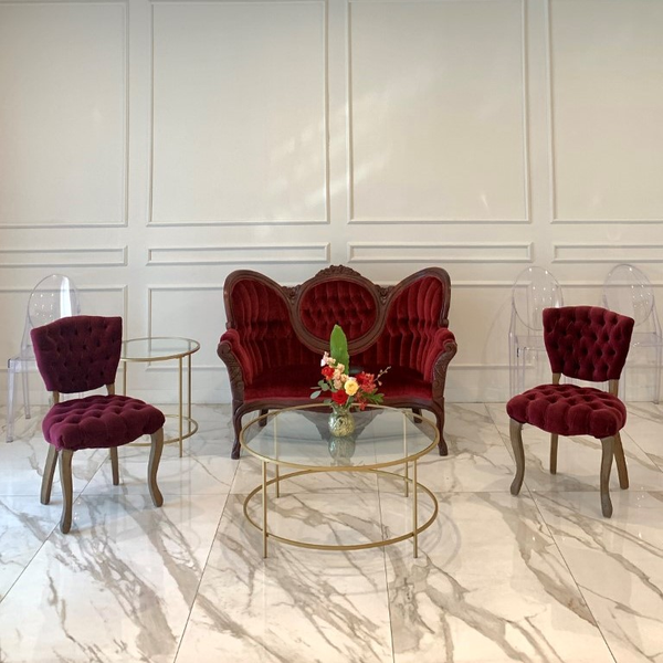 lounge set with burgundy red loveseat with a gold round coffee table with vintage tufted red chairs on each side of the coffee table with side table.