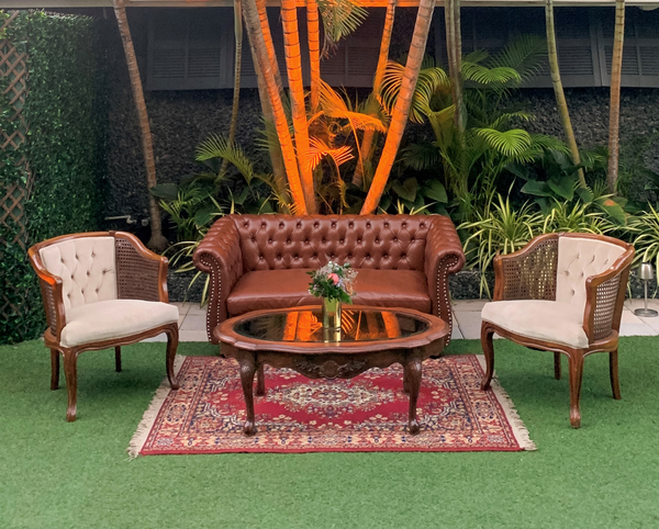 Vintage Mid-century leather tufted brown loveseat with wood legs lounge with a red patterned rug, a brown wood coffee table and wood and ivory tufted chairs. 