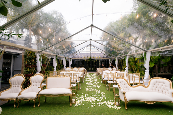 Vintage linen tufted ivory beige sofa with gold accents in a row of upholstered lounge pieces and sofas creating an aisles parted in the middle by flower petals. 