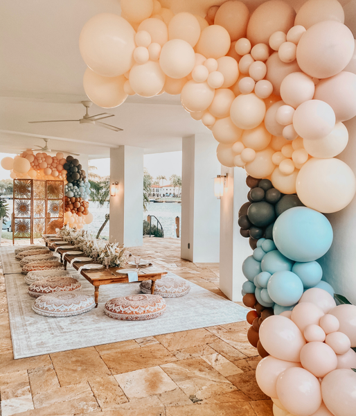 Vintage rectangular ivory beige rug under a wood picnic table with floor pillows surrounding it and a balloon garland on the side of it. 