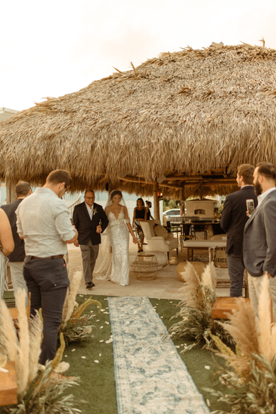 vintage blue rectangular runner rug down an aisle with chairs and people on either side and a man and woman headed towards the runner. It is outdoors. 