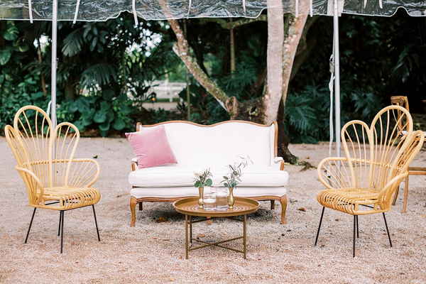 Modern vintage linen ivory beige loveseat with wood accents with boho rattan floral shaped chairs and a bronze gold coffee table in the center. 