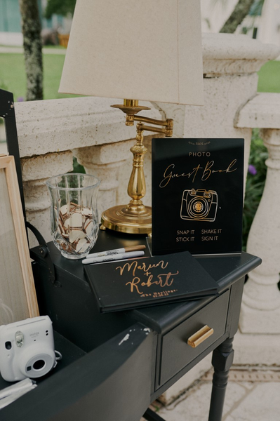 Vintage black rectangular dresser accent table with a polaroid camera, book and sign with writing on it. 