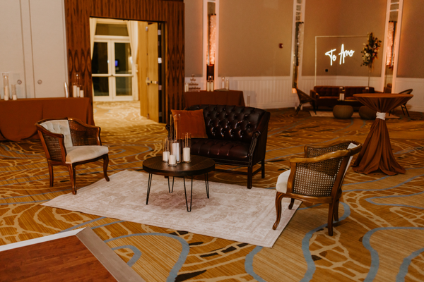 lounge set with leather brown sofa with a brown wood coffee table with vintage beige wood arm chairs on each side of the coffee table on a beige patterned rug.