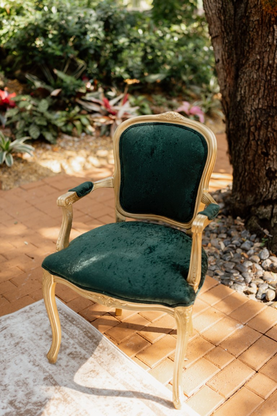 Vintage velvet emerald green arm chair with gold accents outdoors.