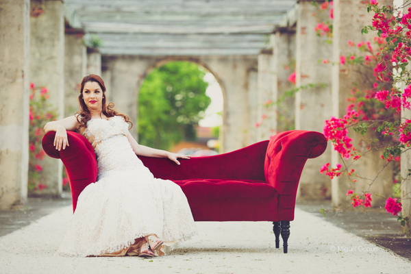 Vintage velvet tufted ruby red assymetrical sofa with wood legs with a woman sitting on it outdoors. 